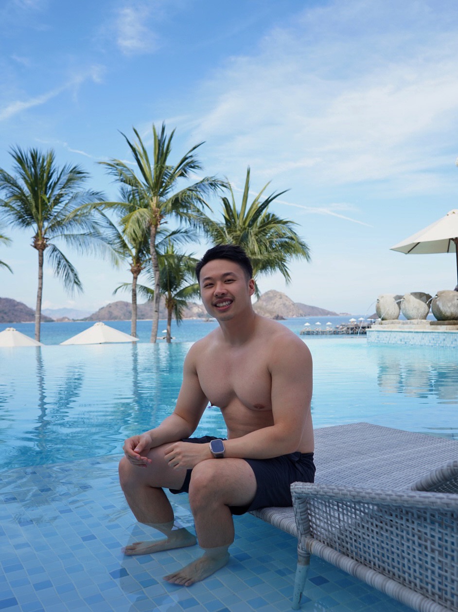 Andy sitting beside a tropical pool beneath palm trees